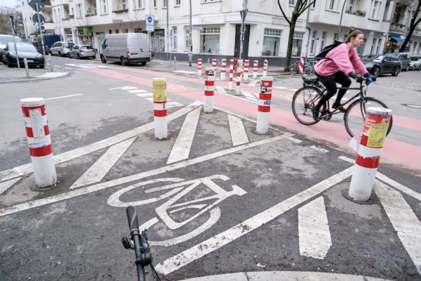 Person riding a bike past a bike crossing with bollards and white paint markings on the ground.